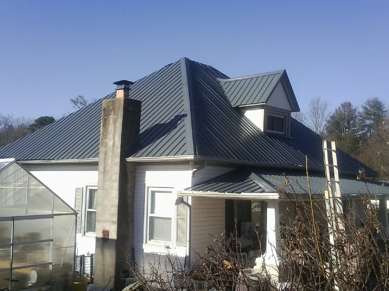 Dark blue standing seam metal roof on a white farmhouse with dormer — Slate & Tile Roof Repair by Roofing Brothers in Newberry