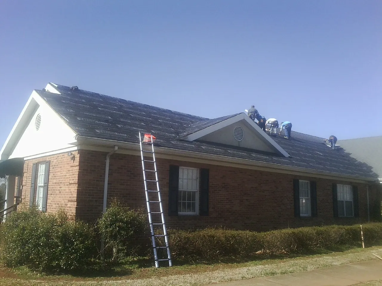 Crew tearing shingles off a brick ranch roof with a ladder set — Emergency Roof Repair work by our crew in Newberry