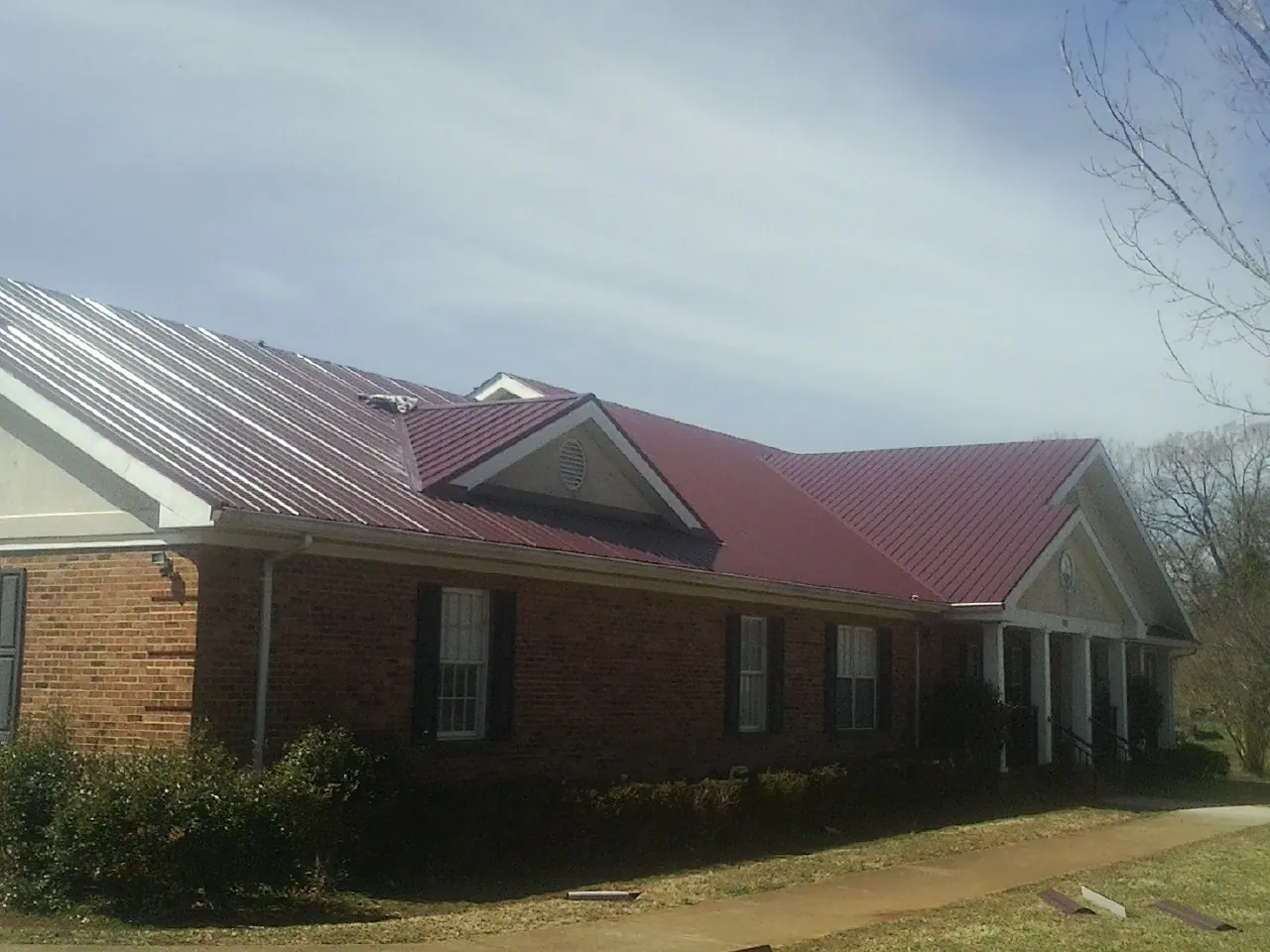 Red metal roof with gabled entries on a long brick building, from a Hail Damage Roof Repair job in Newberry